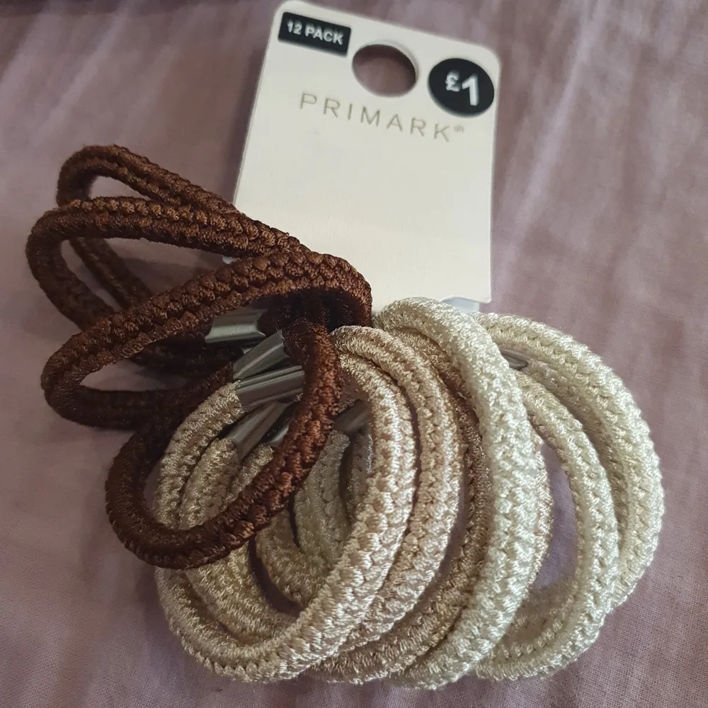 A pack of Primark hair bands in neutral colors, including black, brown, and beige. The hair bands are shown in a variety of sizes, with some in a ponytail and others laid flat.